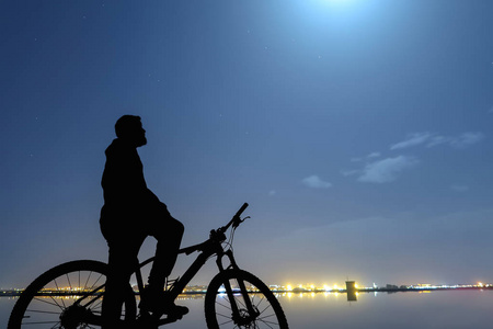 一个年轻男子的剪影在山地自行车寻找月亮与美丽的天空在晚上, 作为抽象背景