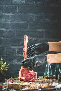 男性手屠夫或厨师持有战斧牛肉牛排在深色质朴的厨房表背景