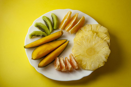 热带水果, 猕猴桃, 芒果, 菠萝, 橙色和柑橘片放在白色的盘子上, 在黄色背景上分离。顶部视图, 平躺
