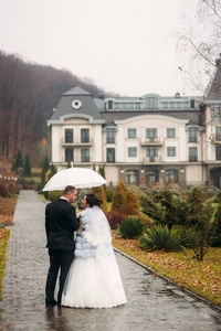 新郎和新娘在婚礼当天在公园散步。秋天的天气。矮人.情侣伞