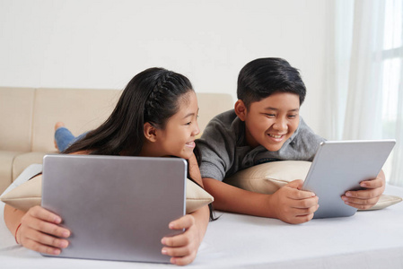 两个亚洲儿童用笔记本电脑和数字平板电脑躺在床上