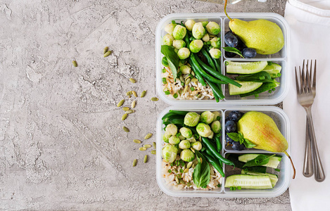 纯素食绿色食品准备容器与米, 青豆, 布鲁塞尔芽, 黄瓜和果子在石头灰色背景