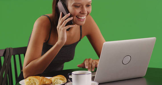 可爱的年轻女子聊天在智能手机上, 而使用在绿色屏幕上的笔记本电脑