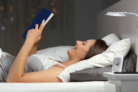 一个快乐的女人在家中晚上躺在床上看书的简介
