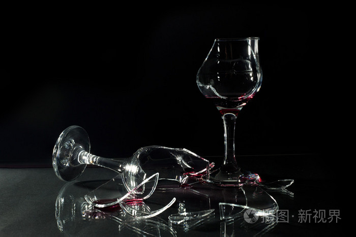 洒上黑孤立的玻璃桌上的碎的玻璃杯子里的红酒