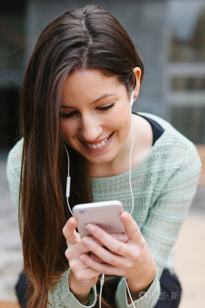一个年轻漂亮的女人听音乐与手机在户外的特写