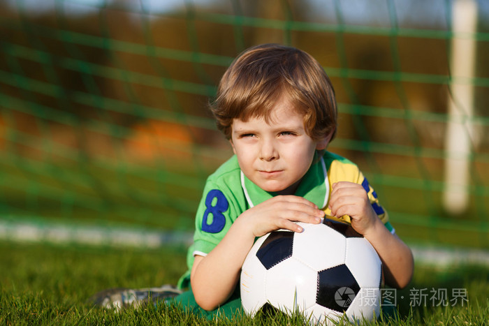 4在足球场踢足球和足球的金发男孩