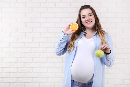 美丽的孕妇与橙色和苹果水果在砖墙背景上