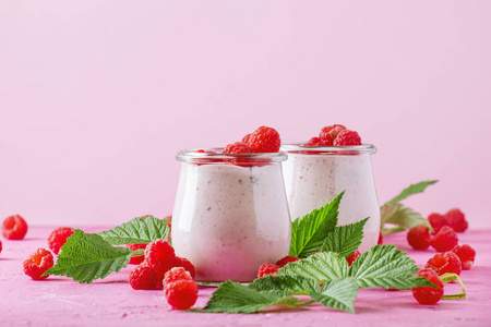 覆盆子冰鲜在玻璃罐子与新鲜的莓果和希腊酸奶在桃红色石头背景, 选择性焦点