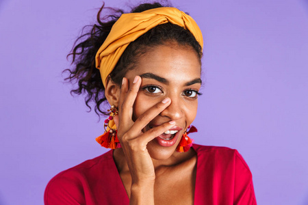 关闭一个快乐的年轻非洲妇女的肖像在带上的紫罗兰色背景, 看着手在她的脸上的相机