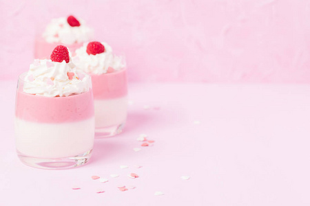 在柔和的粉红色背景上装饰有奶油和心饰的覆盆子智世陶杯关闭美丽的眼镜的夏季水果甜乳制品甜点的照片