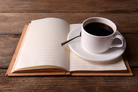 杯碟与笔记本上的咖啡和勺子木桌背景上