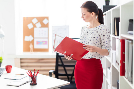 一个年轻的女孩站在办公室, 拿着一个红色的文件夹文件