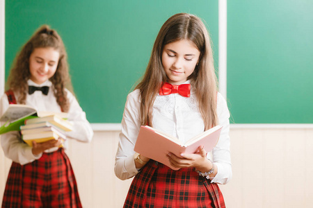 两个滑稽的女生在学校制服是站在学校董事会的背景书
