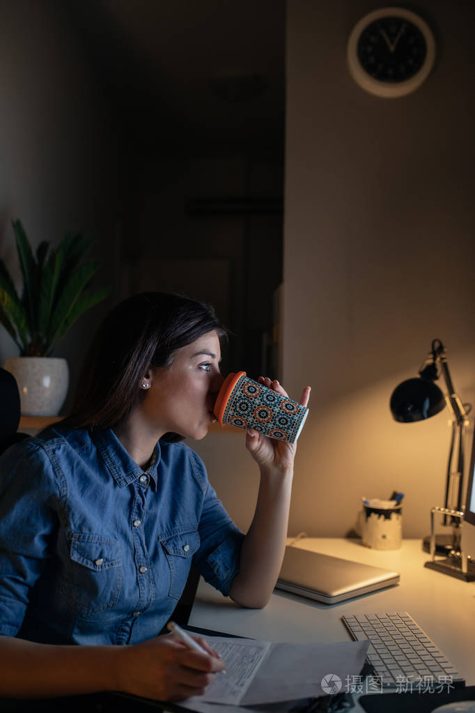 年轻的女商人在家里工作在晚上喝咖啡的肖像