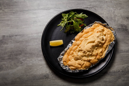 在黑餐馆盘子上用切片柠檬和 rucola 沙拉在灰色桌上吃被烘烤的金鱼的上部看法