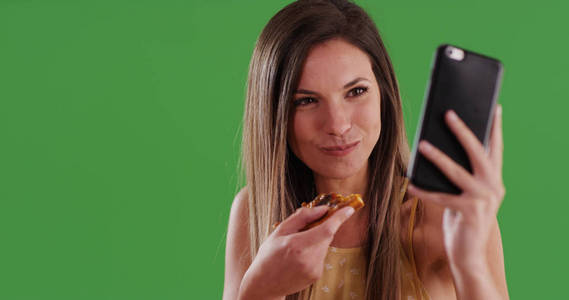 年轻的千禧年白人妇女在绿色屏幕上吃比萨饼时自拍自拍