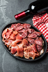 西班牙火腿, 意大利香肠和红酒瓶在石板背景上, 顶部视图