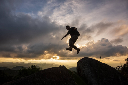 剪影自由青年在日落时在两座岩石山之间跳跃