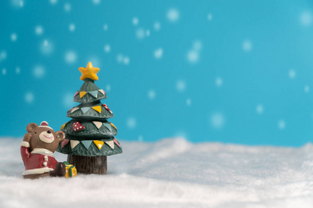 快乐的棕熊穿着圣诞老人礼服与礼物箱子选址在雪附近圣诞树