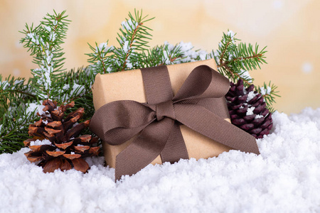 圣诞礼物包裹在棕色纸和丝带与松果和常绿树枝在雪的表面和明亮的背景