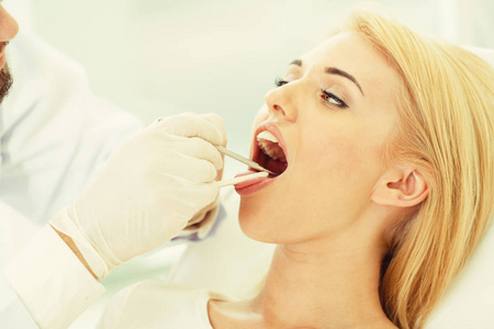 年轻英俊的牙医检查在牙科诊所坐在牙医椅上的快乐妇女病人的牙齿。牙科护理概念