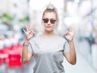 年轻的金发女人戴着太阳镜在孤立的背景下放松和微笑闭上眼睛做冥想手势用手指。瑜伽理念