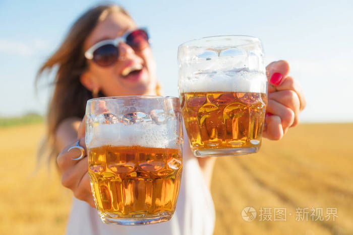在一个大麦田里拿着啤酒杯的快乐女孩光学聚焦在手和玻璃上