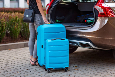 女子把两个蓝色塑料行李箱放在汽车后备箱上.旅行准备照片