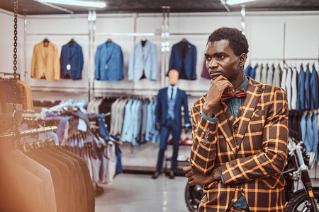 穿着优雅的非洲男子摆着手在下巴, 而站在一个经典的男装店