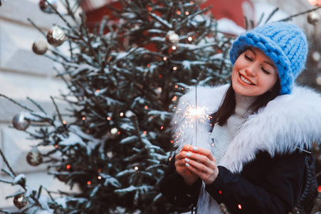 圣诞肖像的快乐女人与燃烧的火光散步户外在雪冬城穿着白色毛皮和特大块针织帽子的时尚大衣