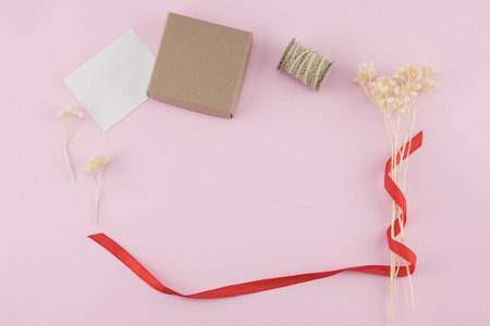 空白白色卡片, 褐色礼物盒和绳索装饰与白色干花花束在柔和的粉红色背景与拷贝空间