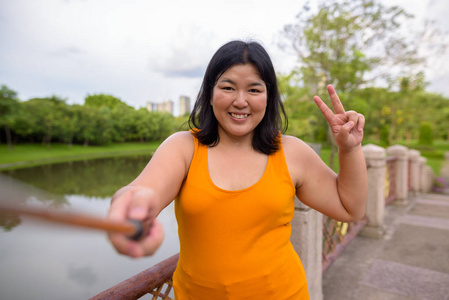 亚洲妇女采取自拍与手机附加到自拍棒在公园