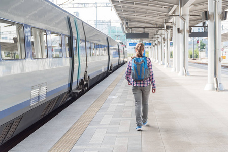 女游客沿着月台走着赶上火车。火车站有蓝色背包的年轻女子。铁路旅行。现代高速列车