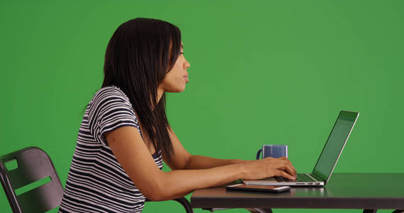 在绿色屏幕上的桌子上工作的黑人妇女的侧视图