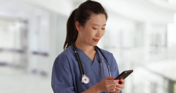 快乐的年轻亚洲医生在擦洗短信与智能手机在空医院内