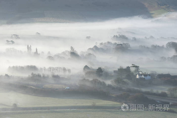 美丽的雾英国乡村风景在日出在冬天与层数滚动通过领域