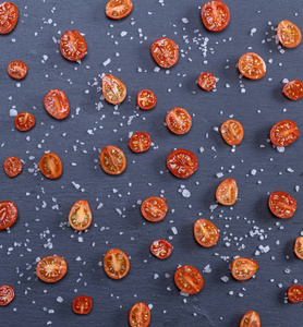 半熟的红色樱桃番茄洒在黑色背景上的盐