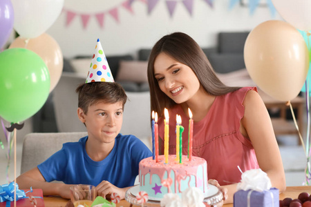 可爱的小男孩和他的母亲在桌与生日蛋糕