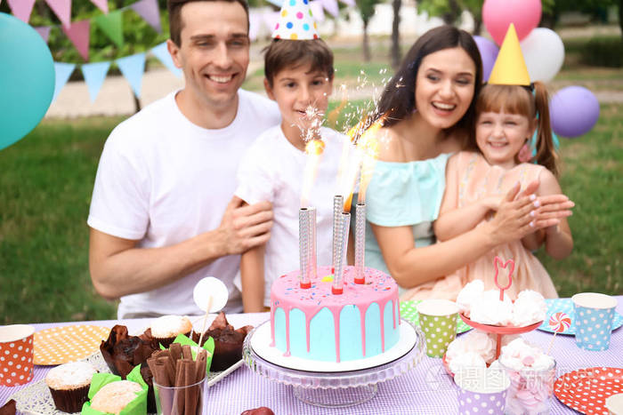 快乐家庭庆祝生日在桌与蛋糕户外