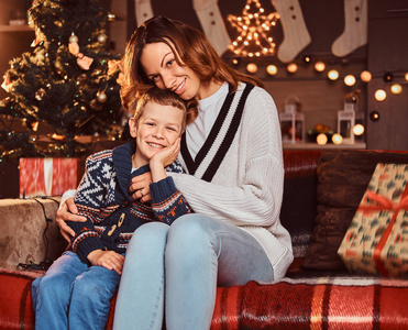幸福的家庭。妈妈拥抱她可爱的小男孩, 而坐在沙发上装饰的房间在圣诞节时间