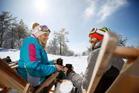 在山上的日光浴床上滑雪的妇女和男子享受与饮料
