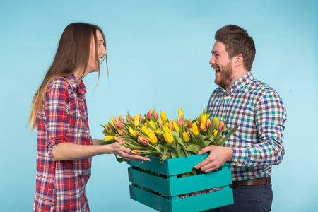 快乐的男人和女人花店举行的郁金香和笑蓝色背景的盒子