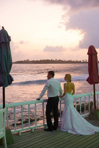 在马尔代夫的热带岛屿海滩上, 新婚夫妇互相拥抱, 观看日落地平线。背景上的绿松石海洋泻湖。蜜月理念