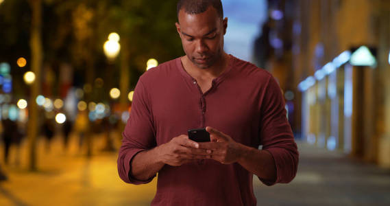 在法国巴黎的香榭丽舍大街上的休闲非洲男人用智能手机发送短信
