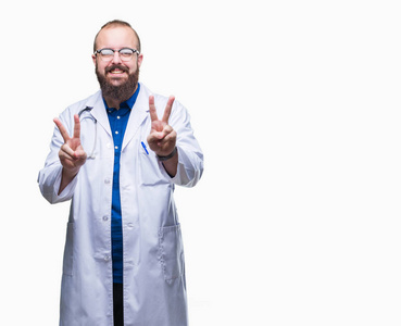 年轻的高加索医生男子穿着医疗白色外套在孤立的背景微笑着看着镜头显示手指做胜利的标志。2号