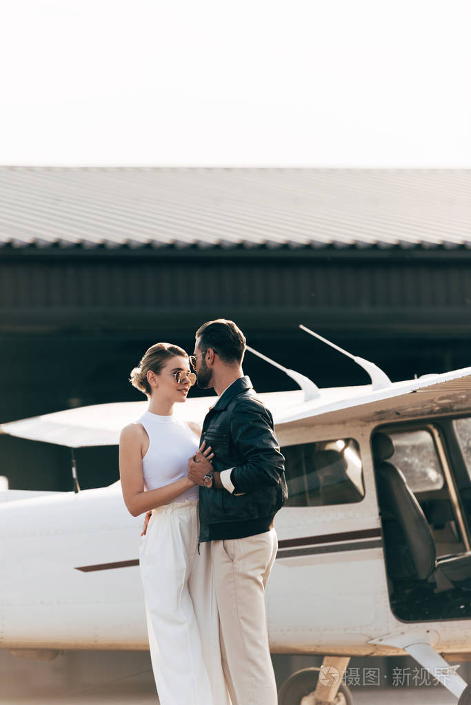 年轻时尚情侣在太阳镜拥抱和站立面对面飞机附近