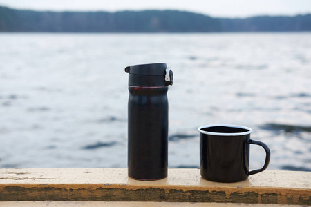 黑色的咖啡杯, 有热水瓶, 背景是湖。概念爱旅行