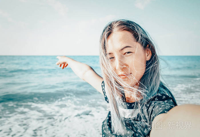 看着相机在海滩和指向大海的快乐的年轻妇女观点