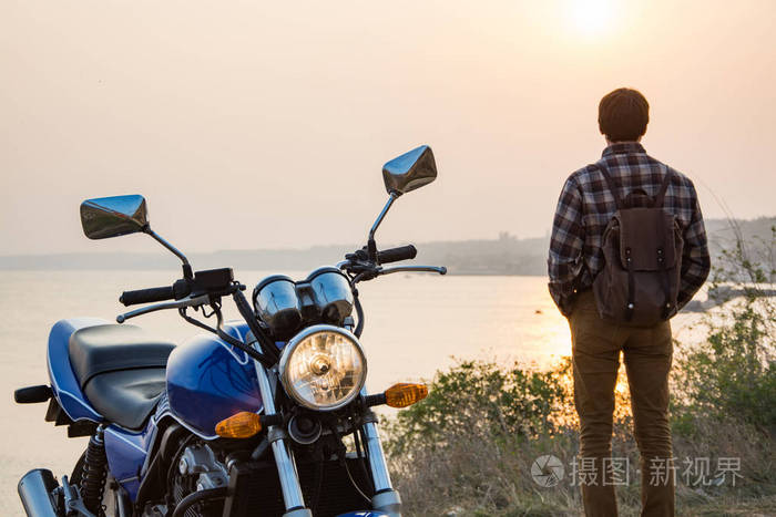 年轻的男性旅行者与摩托车对美丽的夕阳